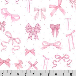 Op de afbeelding: Witte stof met een patroon van roze strikken in verschillende stijlen en maten, sommige met stippen. De strikken zijn verspreid over het oppervlak, met kleine roze stippen op de achtergrond. Onderaan een liniaal.