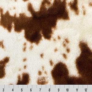 May include: Brown and white cowhide print fabric with a soft, fuzzy texture.