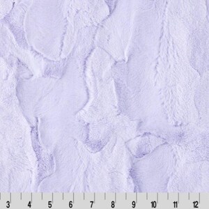 May include: A close-up of a soft, plush fabric in a light lavender color. The fabric has a textured, fuzzy appearance, resembling fur.