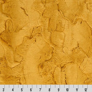 May include: Mustard yellow faux fur fabric with a textured, swirling pattern. The fabric has a soft, plush appearance. A ruler is at the bottom of the image, showing measurements in centimetres.