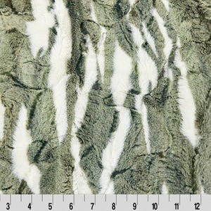 Pode incluir: Close-up de um tecido texturizado com um padrão de listras verticais verde-oliva e brancas. O tecido tem uma aparência macia e felpuda. Uma escala em polegadas é visível na parte inferior.