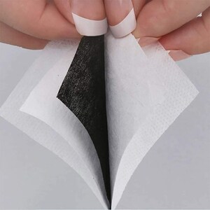 May include: Close-up of a white face mask with a black filter layer. The mask is folded in half, revealing the filter layer.