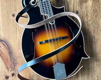 May include: A brown leather strap wraps around a dark brown and amber mandolin with a  "The Loar" logo on the body.