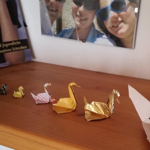 6 Origami Schwäne aus verschiedenem Altpapier in einer Reihe auf einem Regal