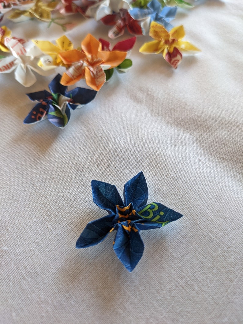 May include: A blue origami flower with yellow and green accents. The flower is made from paper with a printed design.