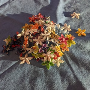May include: A collection of colorful origami flowers made from paper. The flowers are arranged in a pile on a blue fabric surface.