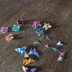 May include: A collection of origami butterflies made from colorful paper. The butterflies are arranged in a variety of positions on a wooden surface.