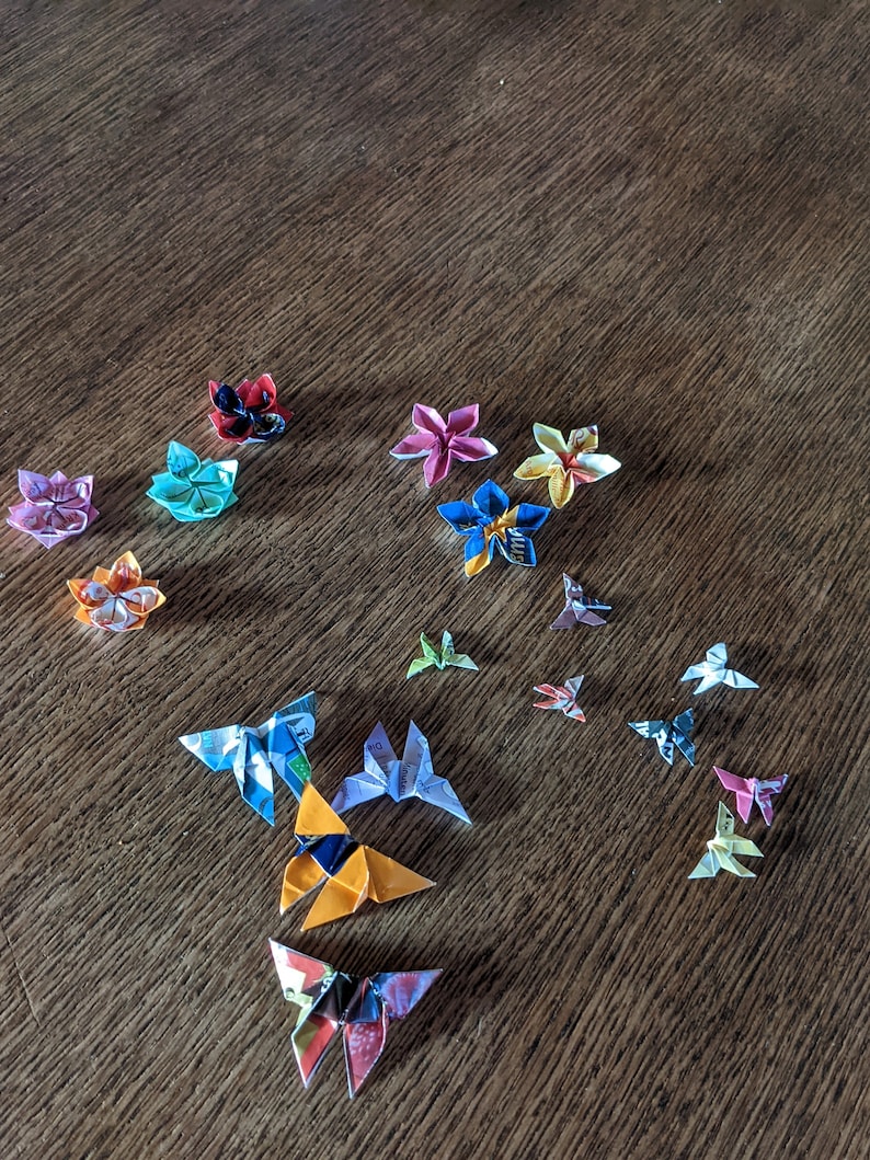 May include: A collection of origami butterflies made from colorful paper. The butterflies are arranged in a variety of positions on a wooden surface.