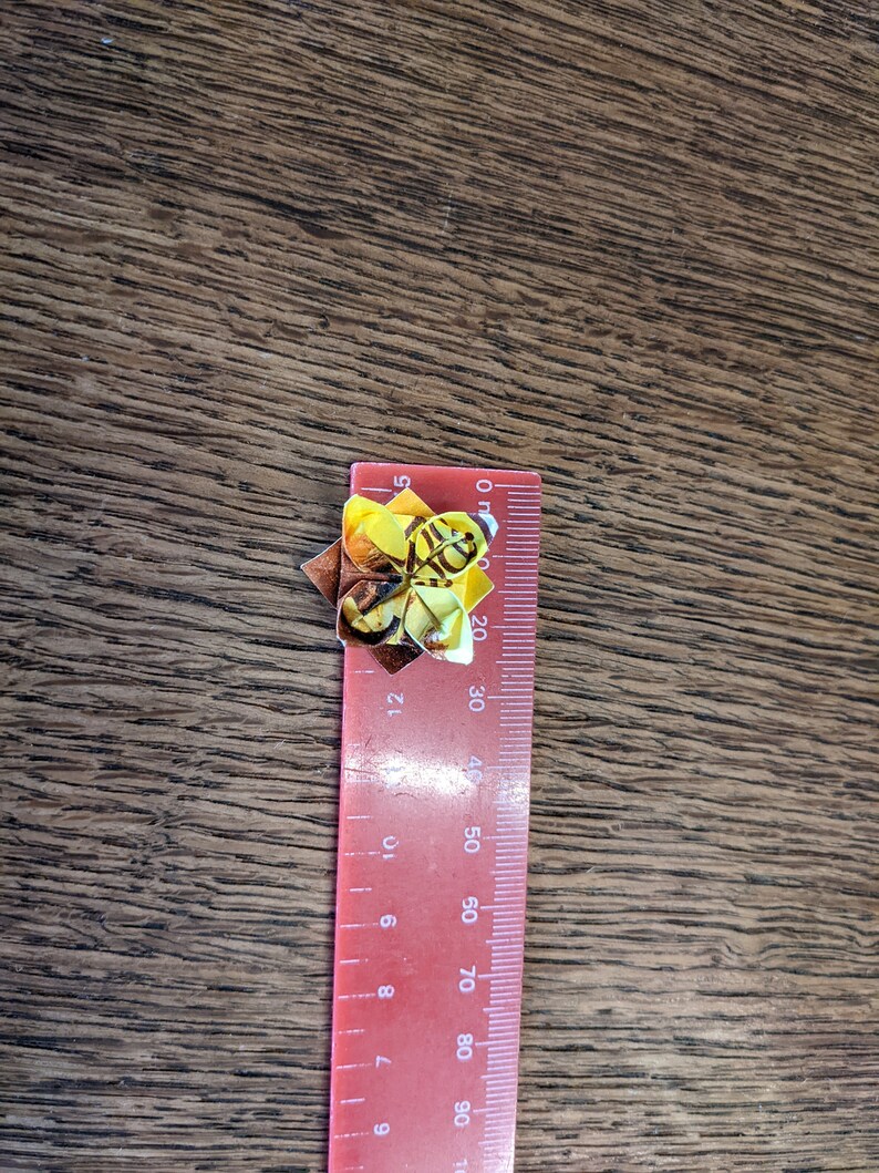 May include: A red ruler with black markings, measuring up to 90 cm, with a yellow and brown origami bee on top.