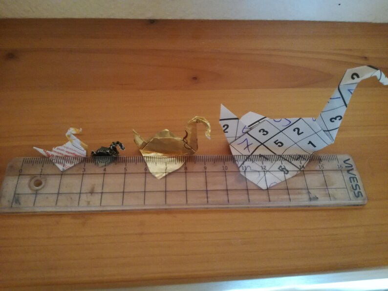 May include: Three origami paper cranes of different sizes. The largest crane is white with black markings and is made from a piece of paper with numbers written on it. The middle crane is gold and the smallest crane is white and red.