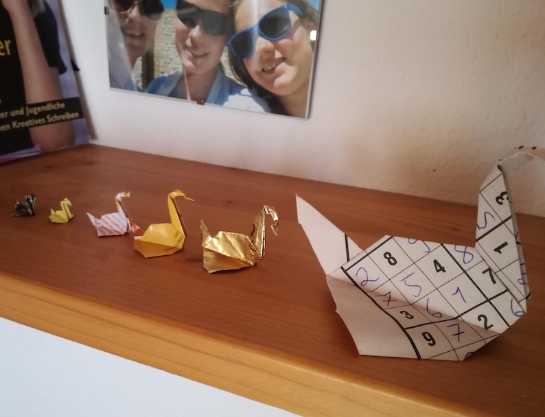 6 Origami Schwäne aus verschiedenem Altpapier in einer Reihe auf einem Regal