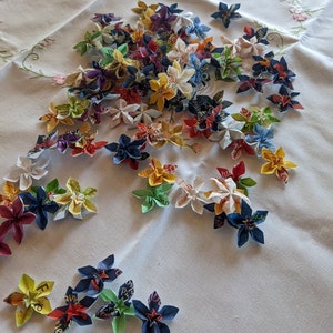 May include: A collection of colorful origami flowers made from paper. The flowers are arranged on a white tablecloth with a floral pattern.