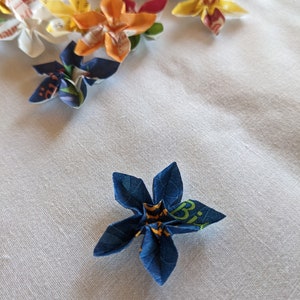 May include: A blue origami flower with yellow and green accents. The flower is made from paper with a printed design.