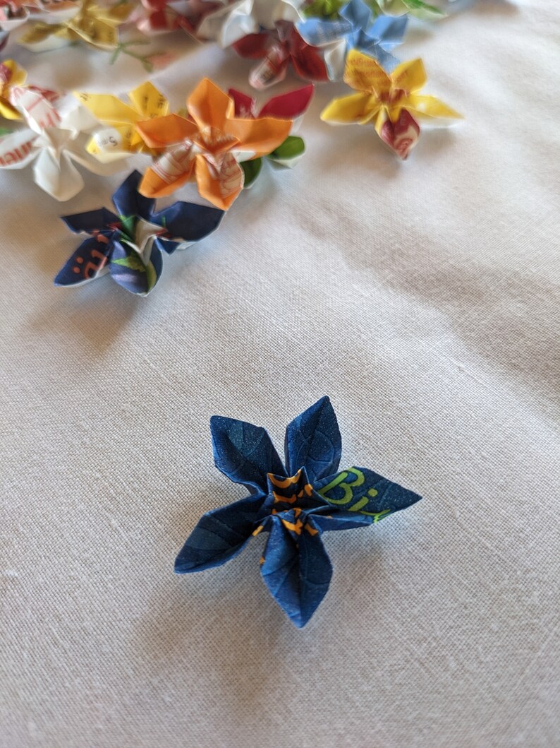 May include: A blue origami flower with yellow and green accents. The flower is made from paper with a printed design.