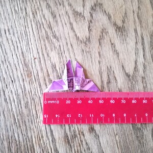 May include: A purple origami butterfly with a ruler underneath. The ruler is marked in millimeters and inches. The butterfly is approximately 4 centimeters wide.