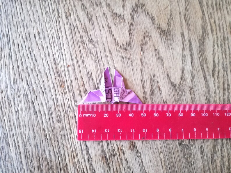 May include: A purple origami butterfly with a ruler underneath. The ruler is marked in millimeters and inches. The butterfly is approximately 4 centimeters wide.
