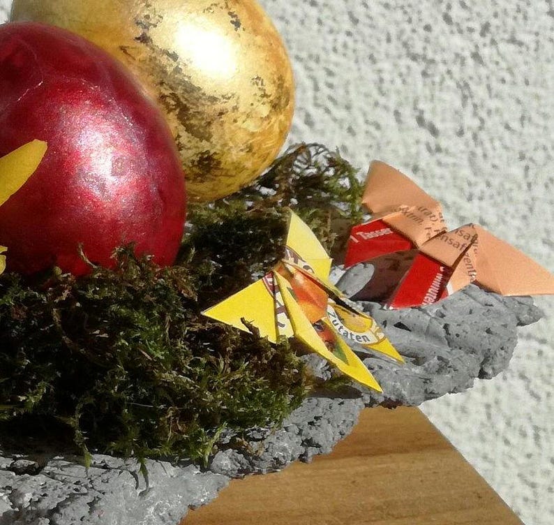 Bunte Origami Schmetterlinge aus verschiedenem Teebeutelpapier. Hier als Oster- oder Frühlingsdekoration in einer Schale mit Feldblumen und Ostereiern.