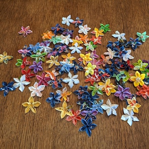 May include: A collection of colorful origami flowers made from paper. The flowers are in various shades of blue, green, yellow, orange, red, and white. The flowers are arranged in a loose cluster on a wooden surface.