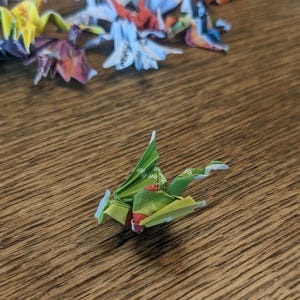 May include: A green origami dragon with red and white accents. The dragon is made from paper and is folded into a traditional Japanese style.
