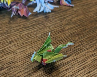 Puede incluir: Un dragón de origami verde con acentos rojos y blancos. El dragón está hecho de papel y está doblado en un estilo japonés tradicional.