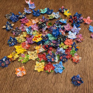 May include: A collection of colorful origami flowers made from paper. The flowers are in various shades of blue, red, yellow, green, and purple. They are arranged in a cluster on a wooden surface.