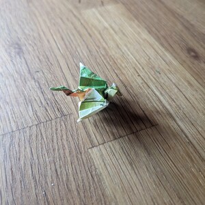 Może przedstawiać: Zielony i brązowy smok origami, złożony z papieru, na drewnianej powierzchni.