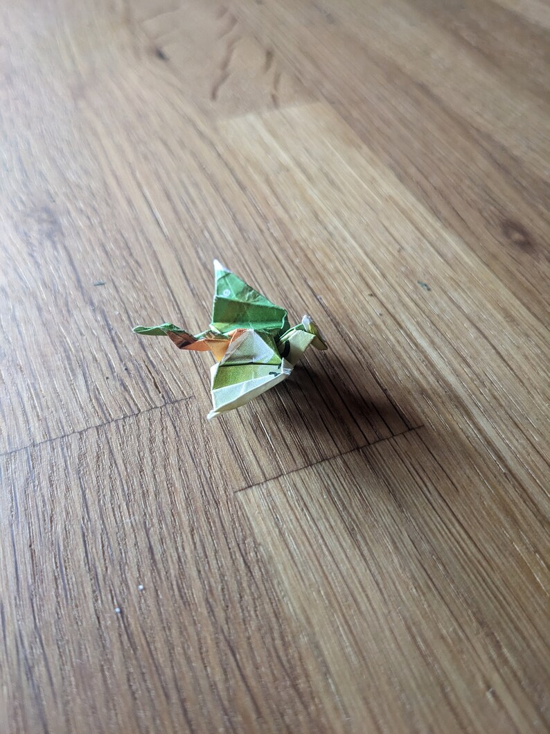 Może przedstawiać: Zielony i brązowy smok origami, złożony z papieru, na drewnianej powierzchni.