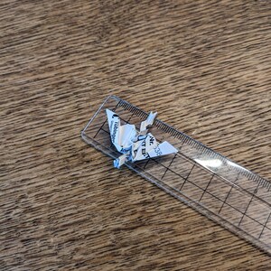 Może przedstawiać: Biały żuraw origami wykonany z kawałka papieru z tekstem "Luhnsdorf" i "Unternehmer" na nim. Żuraw siedzi na przezroczystej plastikowej linijce z czarnymi oznaczeniami.