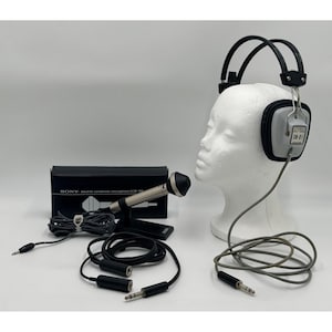 Puede incluir: Un micr&oacute;fono de condensador electret Sony ECM-16B en una caja negra, una cabeza de maniqu&iacute; blanca con auriculares est&eacute;reo grises y negros etiquetados como SN-01, y varios cables de audio negros con conectores met&aacute;licos para equipos de sonido.