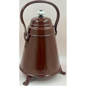 Könnte beinhalten: Eine braune Emaille-Teekanne mit gebogenem Griff und einem weißen und blauen Blumenknauf. Die Teekanne hat eine konische Form und steht auf drei kleinen Beinen. Es ist ein Vintage-Küchenartikel.