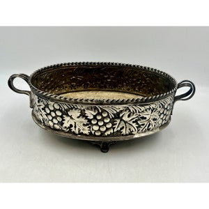 May include: A silver serving dish with a grapevine design. The dish has two handles and sits on three feet.