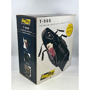 May include: A box for a Bag Boy T-960 premium wheeled travel cover. The box is white with black and yellow text and graphics. The cover is black and has straps and a zippered compartment. The box also shows images of the cover.