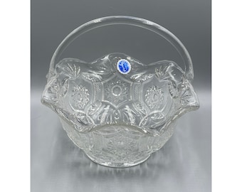 May include: A clear glass basket with a scalloped edge and a handle. The basket has a decorative pattern and a blue label that says "Sprinkle".