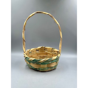 May include: A woven basket with a natural brown handle and a green and brown woven base. The basket is empty.