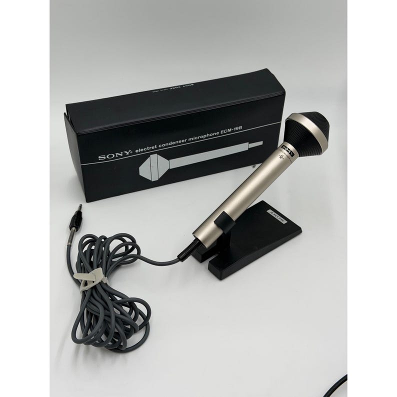 Puede incluir: Un micr&oacute;fono de condensador electret Sony ECM-198 con cuerpo met&aacute;lico plateado y cabezal negro, montado sobre un soporte negro. El micr&oacute;fono incluye un cable gris largo con conector jack y se presenta con su caja rectangular negra original.