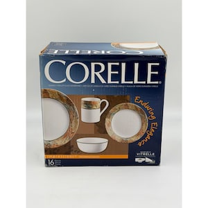 Puede incluir: Una caja de vajilla Corelle de 16 piezas con el patrón Woodland Leaves. El empaque azul oscuro muestra imágenes de una taza blanca, un tazón y dos platos con bordes de hojas en colores otoñales. El texto incluye Corelle, Impressions y Enduring Elegance.