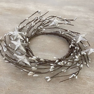 May include: A circular wreath made of brown twigs, adorned with silver glitter stars and small white berries. The wreath is a decorative item, suitable for seasonal or holiday displays.