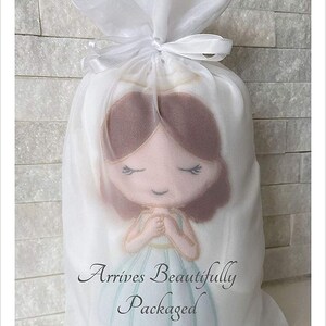 Pu&ograve; includere: Una borsa di organza bianca con un nastro bianco legato in cima. Dentro della borsa c'&egrave; una piccola bambola fatta a mano con i capelli castani, gli occhi chiusi e un vestito azzurro chiaro. La bambola tiene le mani giunte in posizione di preghiera. Il testo "Arrives Beautifully Packaged" &egrave; stampato sulla borsa.