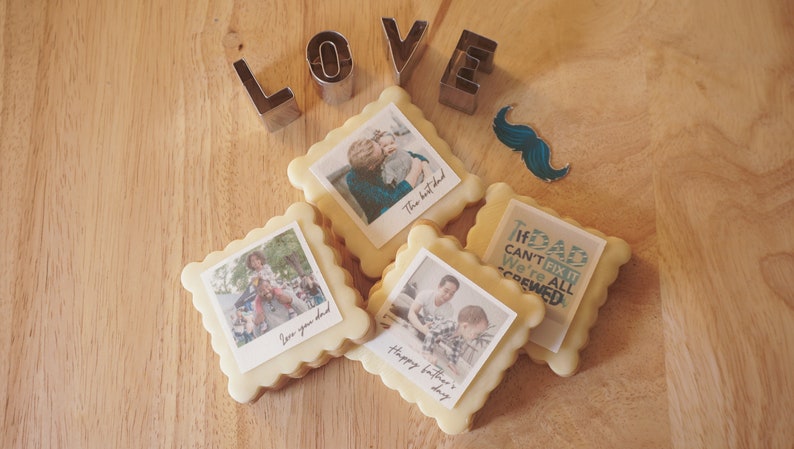 May include: Four decorated sugar cookies with images and text. The cookies are square shaped with rounded edges. The text on the cookies reads "The best dad", "We're all screwed", "Happy Father's Day", and "Love you dad".
