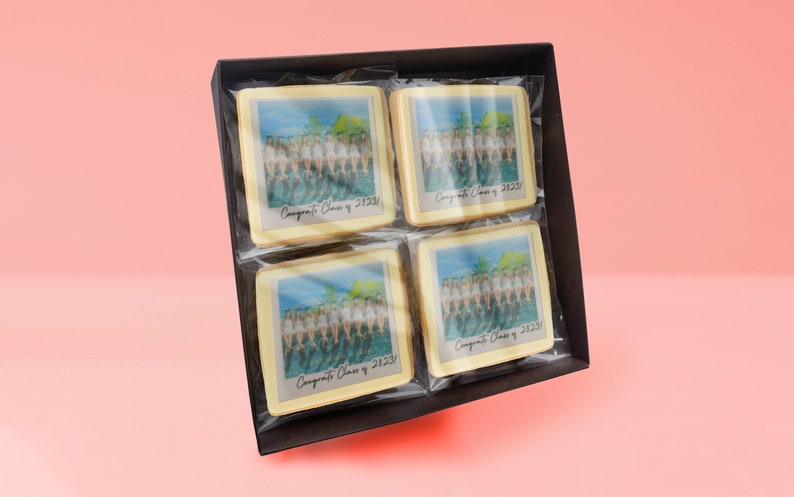 May include: A box of four square cookies, each with a printed image of a group of people and the text "Congrats Class of 2023". The cookies are individually wrapped in clear plastic and presented in a dark brown box.