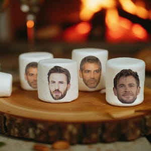 May include: White marshmallows with celebrity faces printed on them are arranged on a wooden serving board. The marshmallows are cylindrical and have images of famous actors. The background includes a blurred fireplace and glasses.