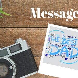 May include: A white photo card with a blue and grey handwritten message that says "The Best Dad!" with blue and grey stars and squiggles around the text.