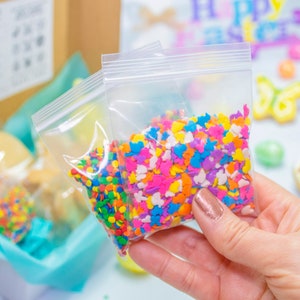 Puede incluir: Tres peque&ntilde;as bolsas de chispas de colores, perfectas para decorar pasteles o galletas. Las chispas son de varias formas, incluyendo corazones, estrellas y mariposas. Las bolsas son de pl&aacute;stico transparente con cierre de cremallera.