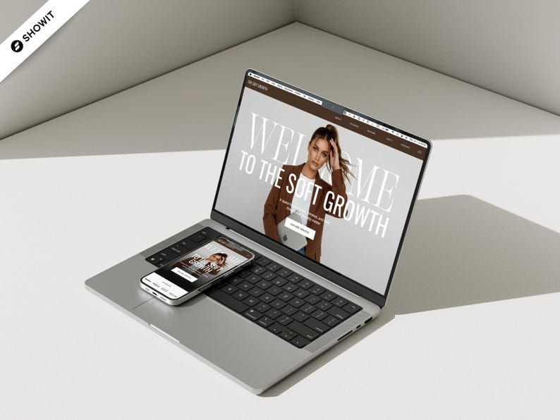 May include: A silver laptop and smartphone displaying a website with the text "WELCOME TO THE SOFT GROWTH". The laptop screen shows a woman in a brown blazer. The smartphone shows a similar image. The devices are on a white surface.