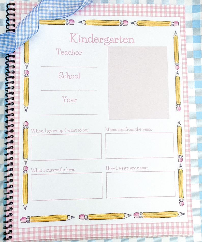 May include: A pink and white gingham patterned journal with a blue ribbon. The cover has a yellow pencil border and the text "Kindergarten" in pink. The journal has blank pages for writing memories from the year.