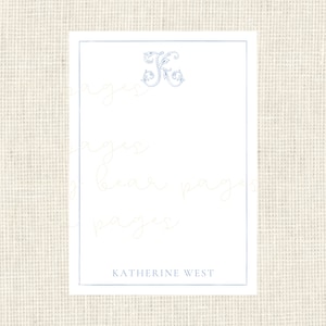 May include: A white card with a blue floral monogram of the letter "K" in the top center. The text "KATHERINE WEST" is printed in blue at the bottom of the card.