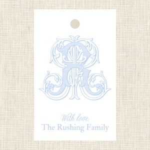 May include: A white gift tag with a blue monogram of the letters "R" and "R" in a decorative font. The text "With love, The Rushing Family" is printed below the monogram.