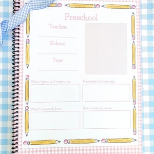 May include: A pink and white checkered background with a white page featuring a preschool memory book. The page has a title "Preschool" and sections for "Teacher", "School", "Year", "When I grow up I want to be", "Memories from the year", "What I currently love", and "How I write my name". The page is decorated with yellow pencils with pink erasers.