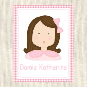 May include: A rectangular card with a pink gingham border and a white interior. The card features a cartoon illustration of a girl with brown hair, a pink bow, and a pink dress. The name "Damie Katherine" is written in pink.