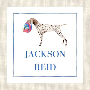 May include: A square card with a blue border features a watercolor illustration of a dog carrying a backpack. The dog has brown and white spots. The name "JACKSON REID" is written in blue, centered below the dog.